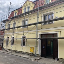 Sebastian Szymczak SzymBud - Żółta, dwupiętrowa kamienica w rusztowaniach, po świeżym malowaniu elewacji. Widoczne detale architektoniczne i numer budynku '33'. Pochmurne niebo w tle.