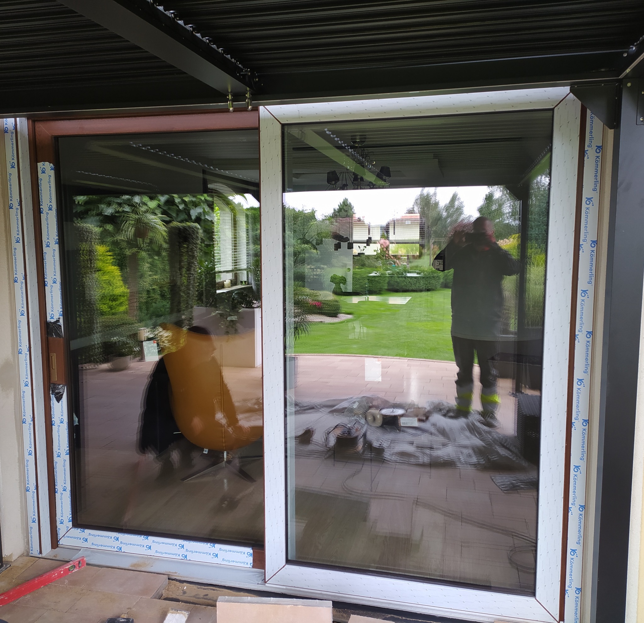 Montaż dwuskrzydłowych drzwi przesuwnych z widocznym profilem Kommerling, poziomica i narzędzia na podłodze. W tle zieleń ogrodu.