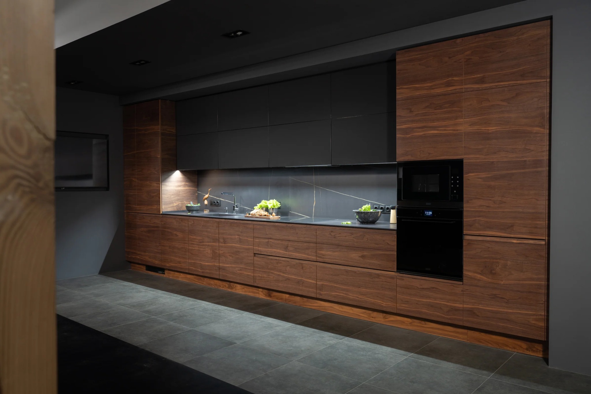 Nowoczesna kuchnia z fornirem orzechowym, czarnymi szafkami górnymi i blatem z efektem marmuru. Oświetlenie LED podkreśla detale. Minimalistyczny design.