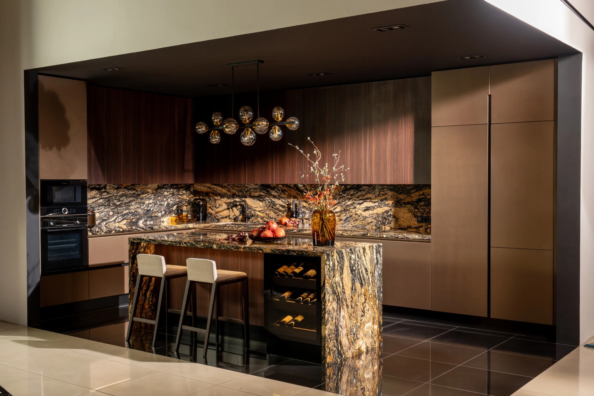 Ekskluzywna kuchnia na wymiar z wyspą wykończoną granitem, oświetleniem punktowym i nowoczesnymi krzesłami barowymi. Widoczny sprzęt AGD w zabudowie.