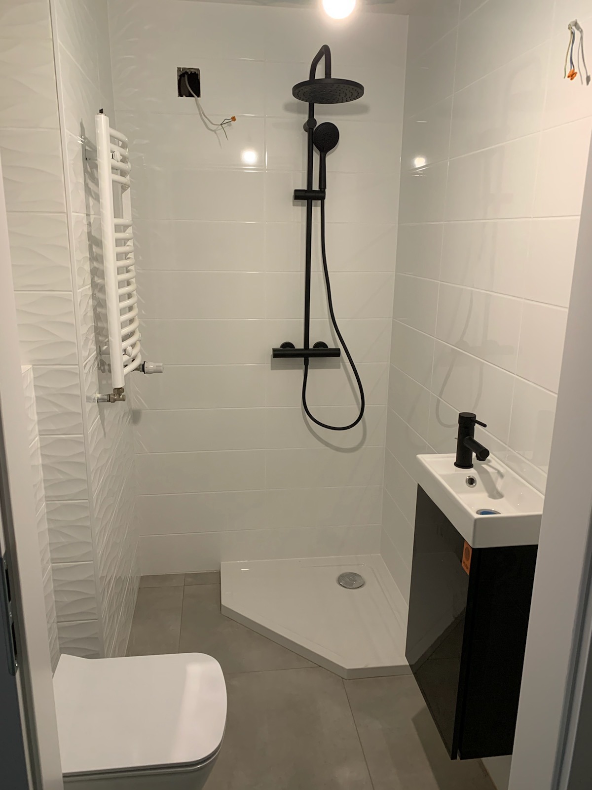 Nowoczesna, biało-czarna łazienka po remoncie. Uwagę przykuwa minimalistyczna kabina prysznicowa z czarną armaturą i mała umywalka z szafką w tym samym kolorze.