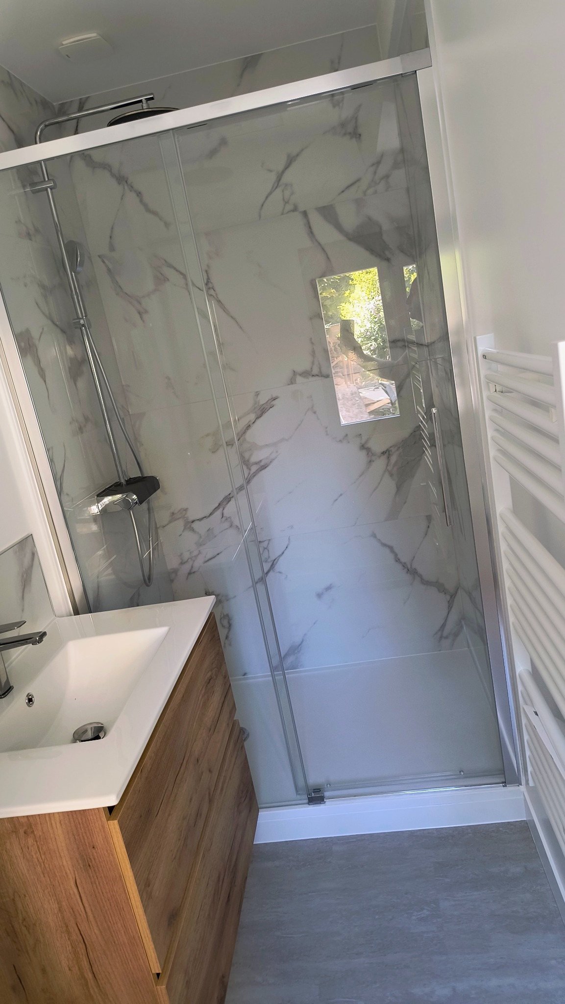 Nowoczesna kabina prysznicowa z marmurowymi płytkami i drewnianą szafką umywalkową. Widoczne detale wykończenia i armatura. Minimalistyczny design.