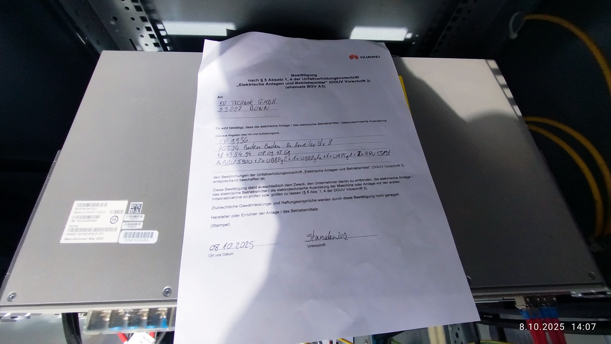 Protokół pomiarów elektrycznych Huawei na tle szafy sterowniczej. Dokument z datą 08.10.2025, podpisany, potwierdzający zgodność instalacji z normami DGUV.