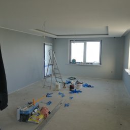 LOS-BUD Łukasz Łosoś - Pokój po malowaniu na szaro, widoczne narzędzia malarskie, drabina i zabezpieczenia. Świeżo pomalowane ściany i sufit z dekoracyjnym elementem.