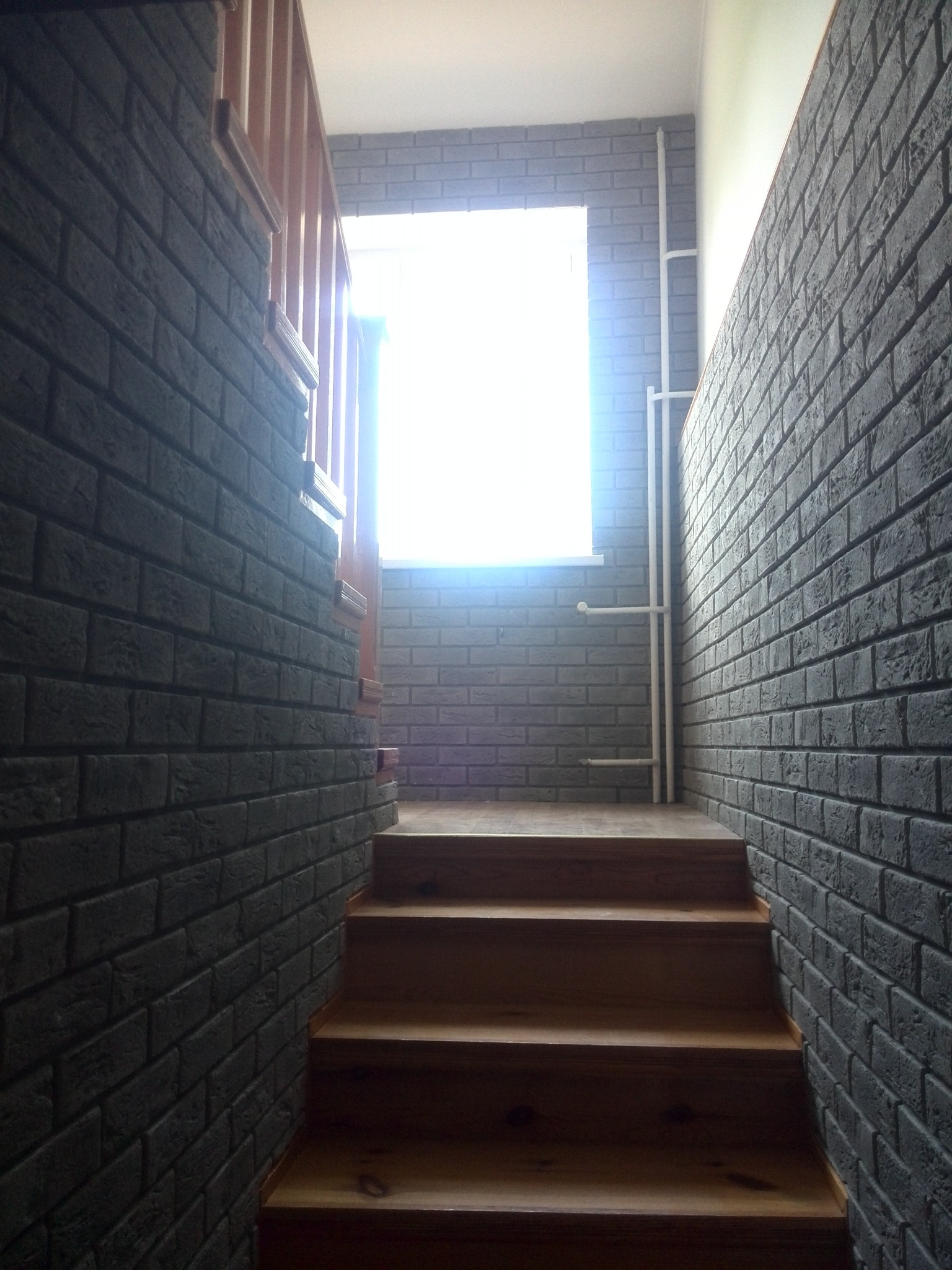 Klatka schodowa z ceglanymi ścianami w Łobżenicy. Widoczne drewniane schody i okno z intensywnym światłem. Dekoracyjne wykończenie ścian.