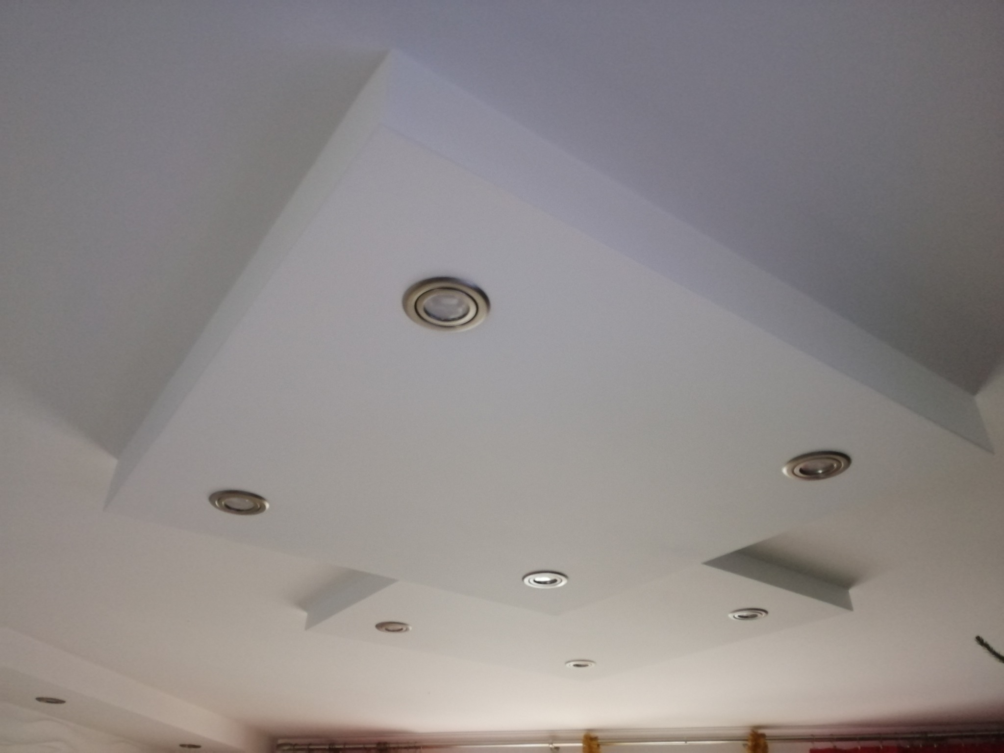 Biały sufit podwieszany z wbudowanymi punktami świetlnymi, widok z dołu, asymetryczny kształt, nowoczesny design, oświetlenie halogenowe.