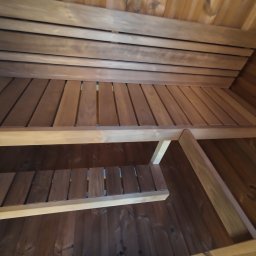 Holzuniversum - Wnętrze sauny z drewnianymi ławkami i boazerią, widok z dołu, ukazujący konstrukcję i detale wykończenia. Ciepłe oświetlenie podkreśla naturalny kolor drewna.