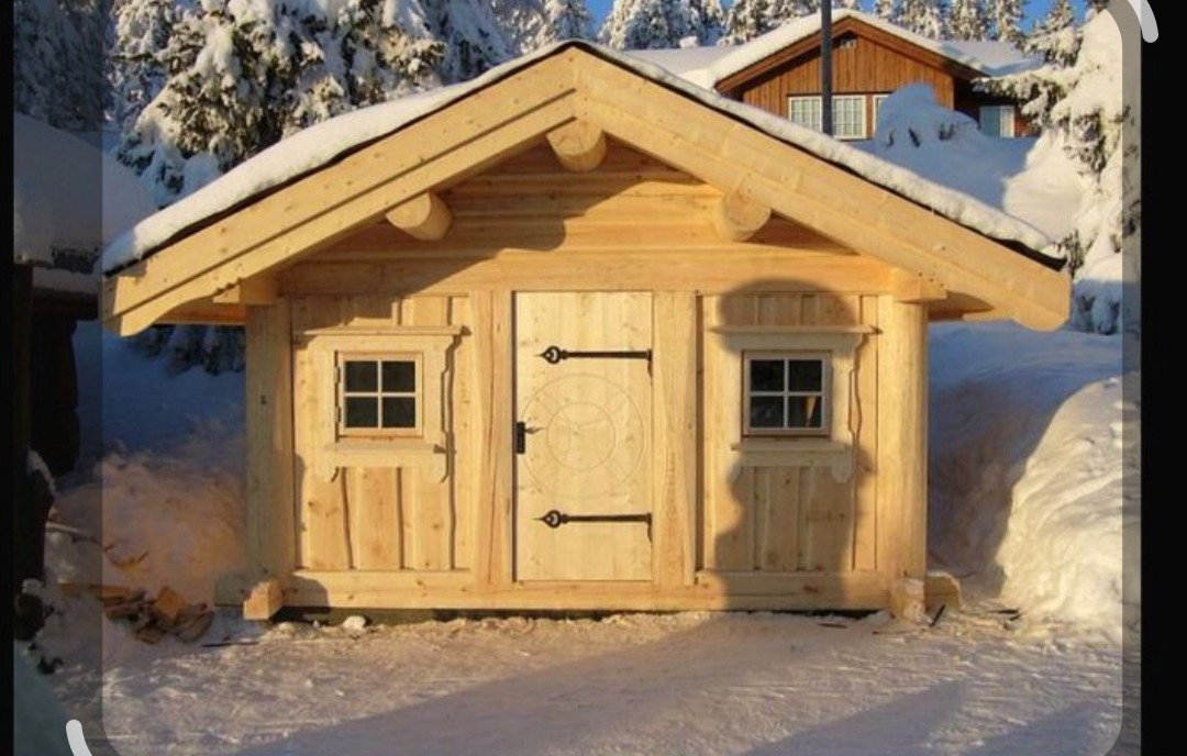 Surowa, drewniana sauna w zimowej scenerii. Widoczne małe okna i drzwi z dekoracyjnym wzorem. Śnieg na dachu i wokół budynku.