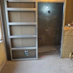Usługi Remontowo Budowlane Maciej Burz - Konstrukcja metalowa z płytami gipsowymi w trakcie montażu, widoczne instalacje w ścianie. Prace wykończeniowe w łazience, surowy stan.