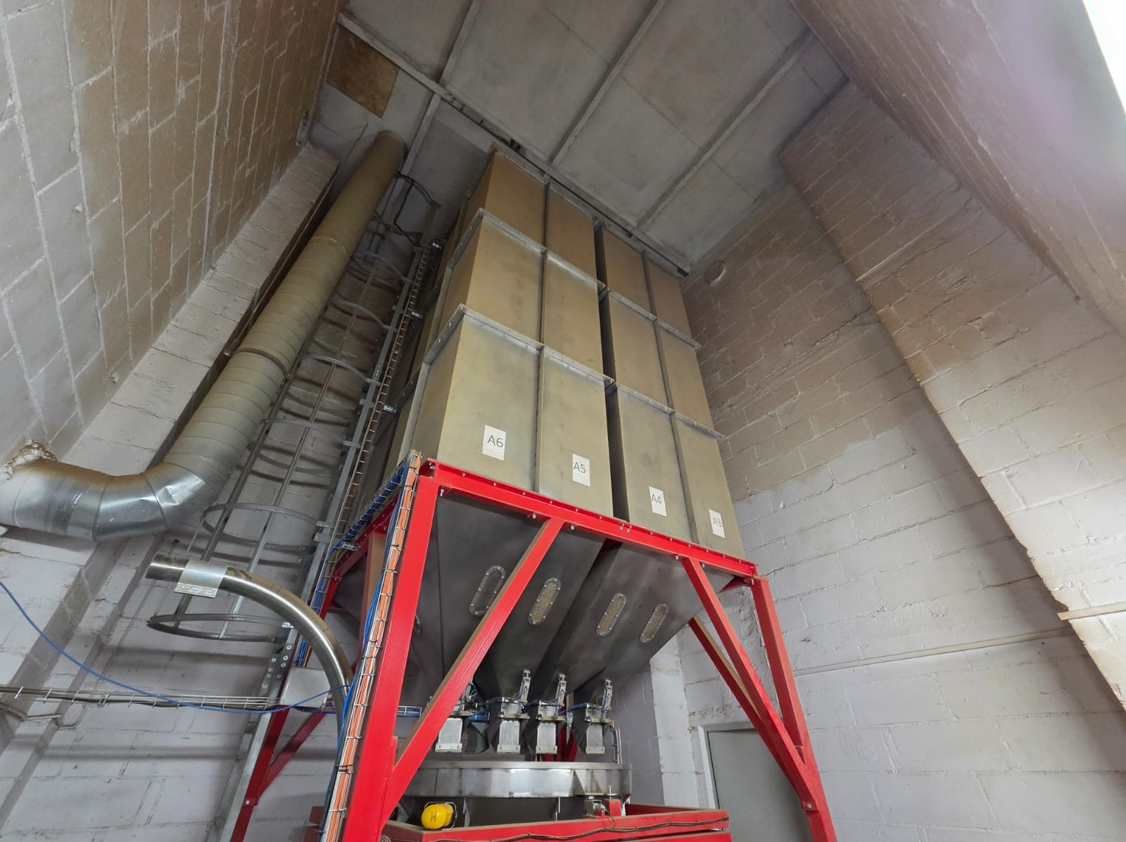 Wysoka konstrukcja z metalu i zbiorników w pomieszczeniu o skośnych ścianach z cegły. Widoczne rury wentylacyjne i drabina. Zbiorniki oznaczone A3, A4, A5, A6.