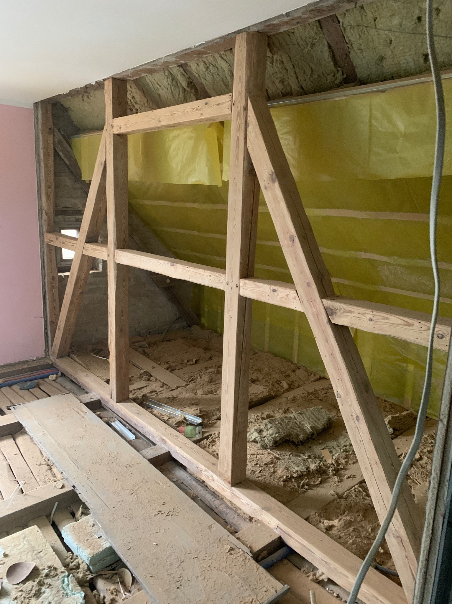 Drewniana konstrukcja szkieletowa w trakcie budowy ściany działowej, widoczne ocieplenie i folia paroizolacyjna. Fragment instalacji elektrycznej.