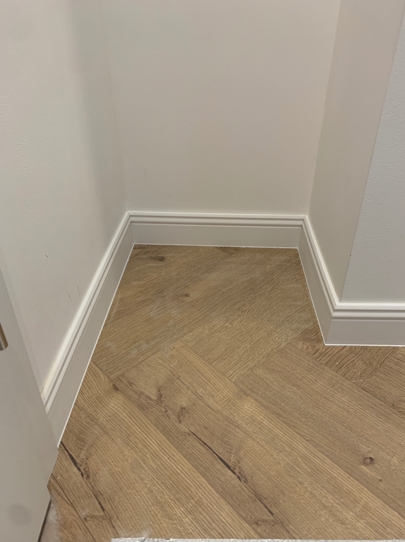 Ukończone wykończenie podłogi z wzorem jodełki, listwy przypodłogowe w narożniku, kremowe ściany. Detal wykończenia wnętrza.