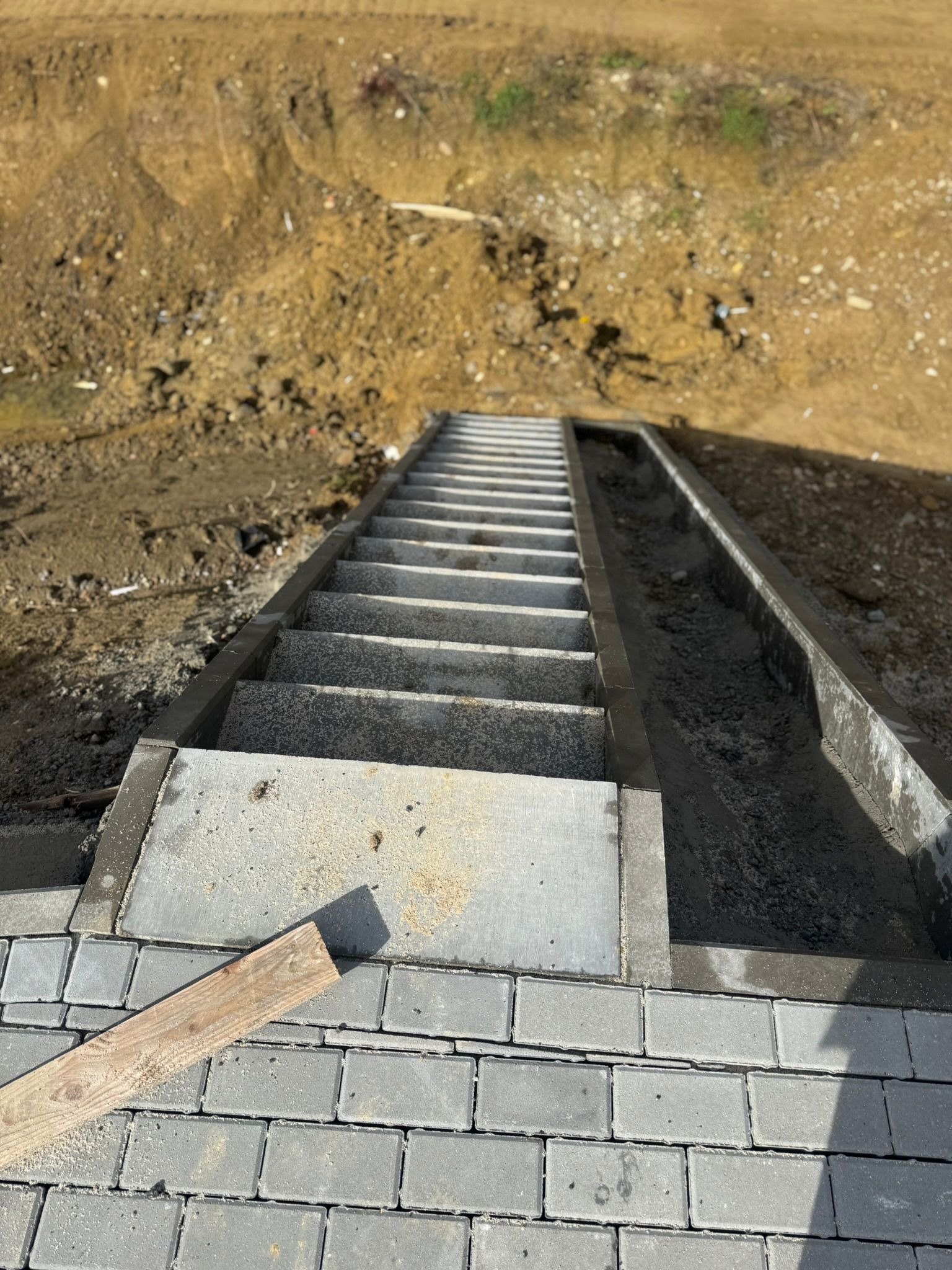 Schody z kostki brukowej prowadzące w dół zbocza, z widocznym korytkiem odwadniającym. Realizacja we Włoszczowie.