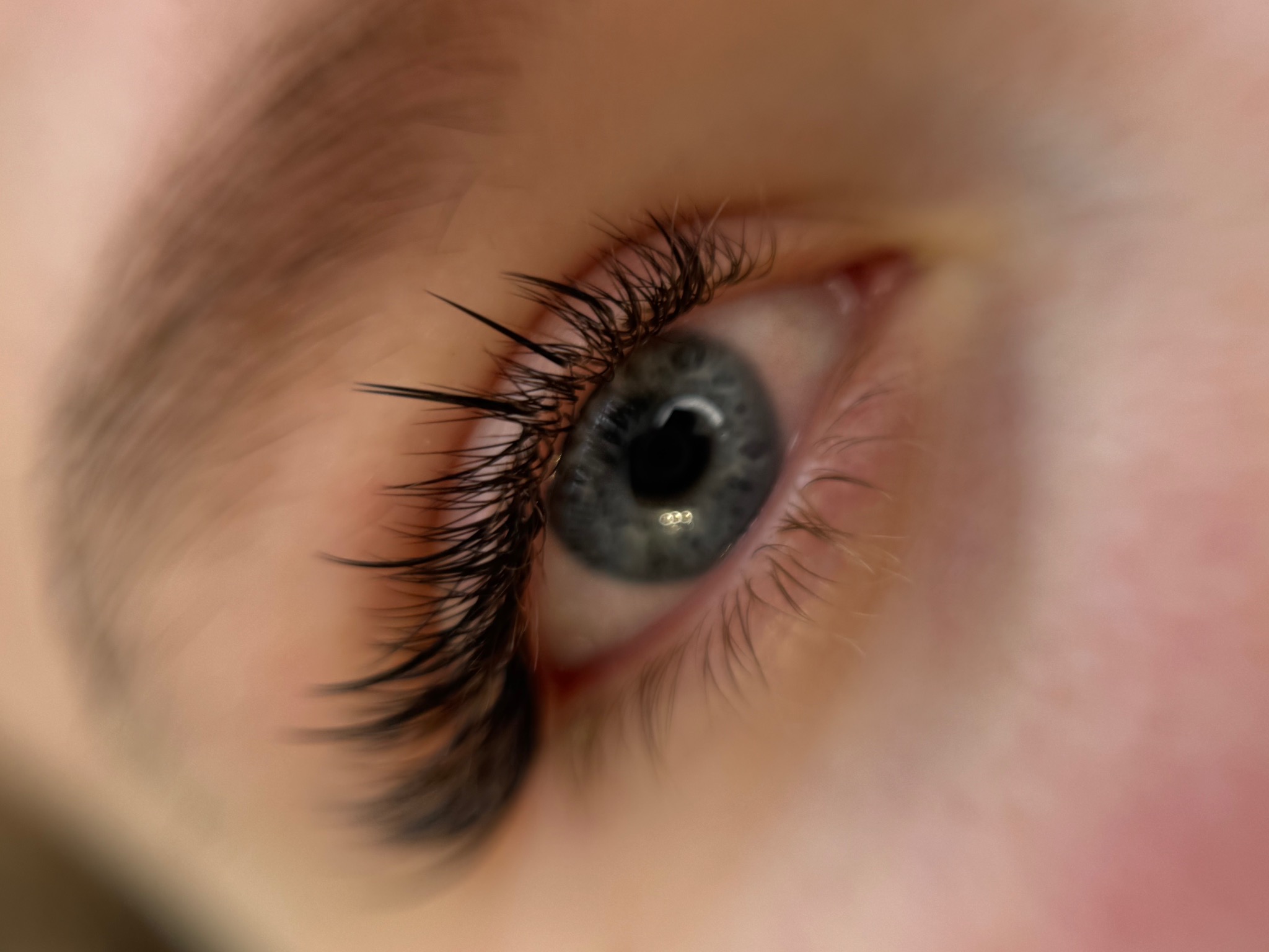 Zbliżenie na oko z wyraźnie przedłużonymi, ciemnymi rzęsami, wykonanymi metodą 2-1 + kim, na tle jasnej skóry. Widoczny efekt stylizacji rzęs.