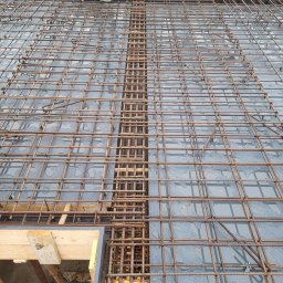 Maciej Warczak - Zbrojenie płyty fundamentowej z widocznym, gęstym układem prętów stalowych i fragmentem szalunku. Prace przygotowawcze do wylewania betonu.