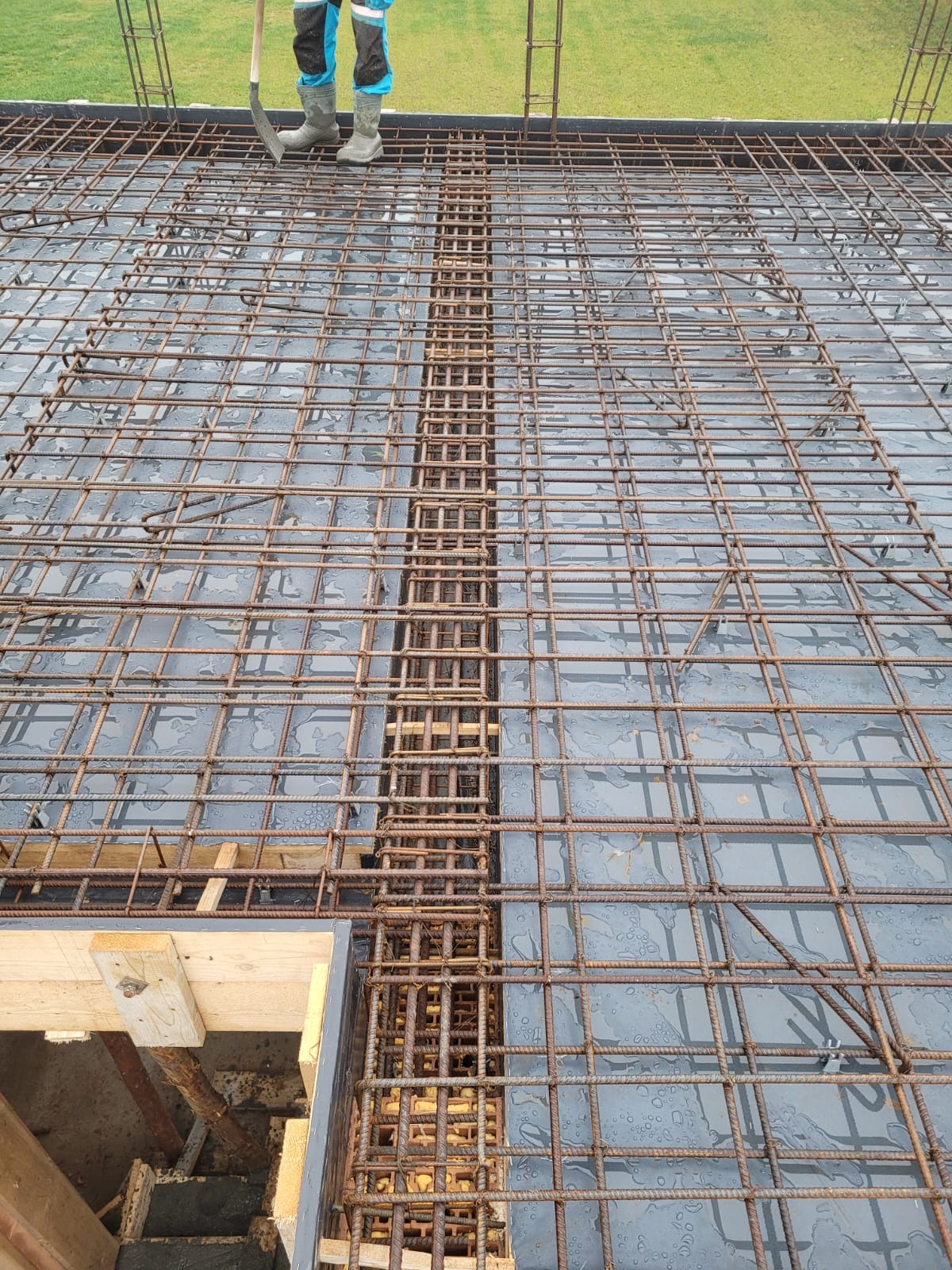 Zbrojenie płyty fundamentowej z widocznym, gęstym układem prętów stalowych i fragmentem szalunku. Prace przygotowawcze do wylewania betonu.
