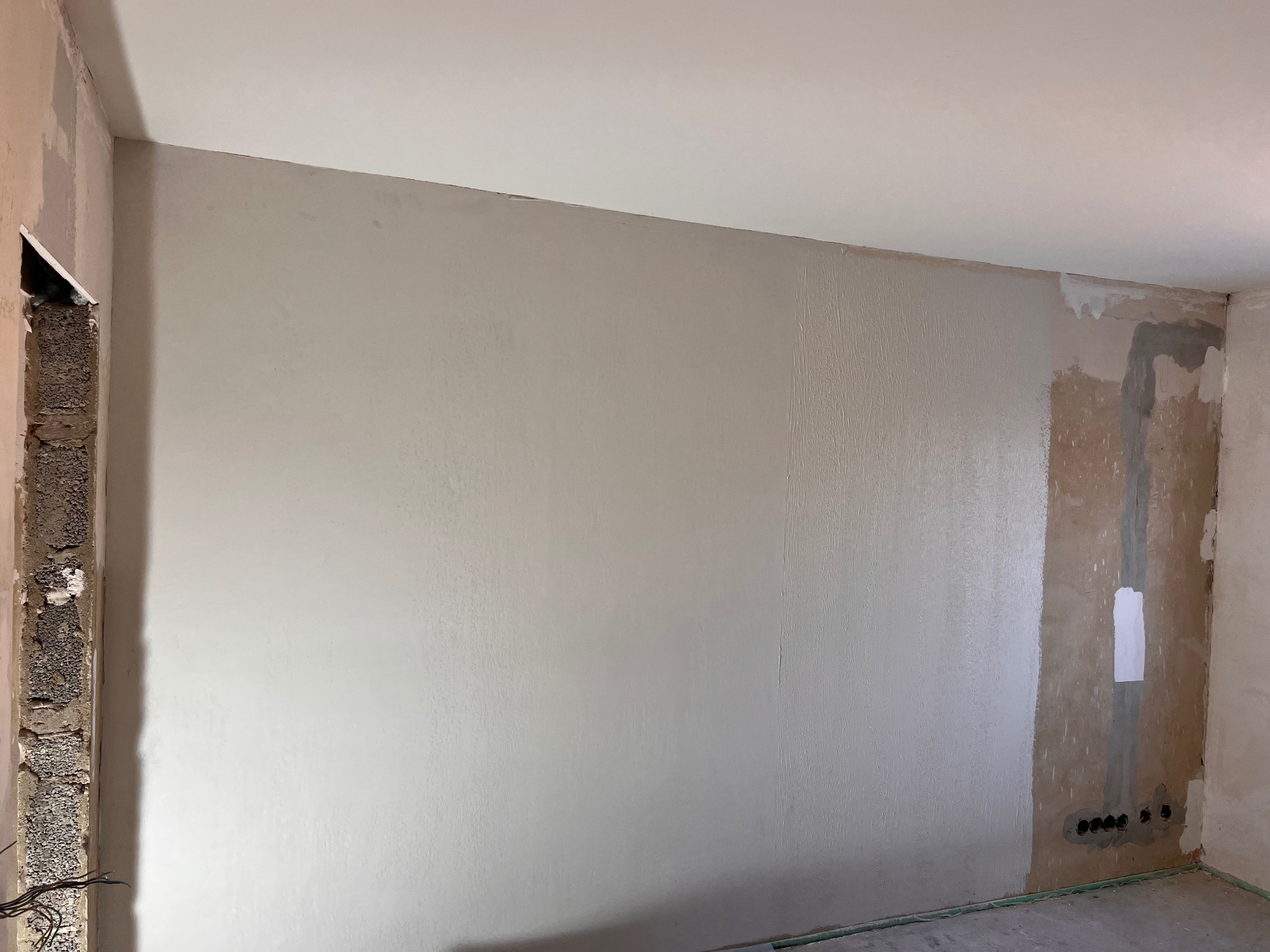 Wnętrze w trakcie gładzenia ścian z widoczną flizeliną, przygotowane do malowania. Fragment ściany z instalacją elektryczną. Surowy stan wykończenia.