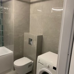 Danch Danylo Muzyka - Wykończona łazienka w szarościach: podwieszana toaleta, pralka Electrolux, płytki imitujące marmur, oświetlenie LED. Minimalistyczny design, nowoczesne rozwiązania.