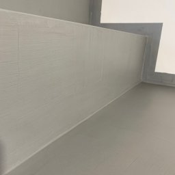 Danch Danylo Muzyka - Szare, świeżo pomalowane ściany i podłoga w rogu pomieszczenia, widoczne ślady pędzla, biały fragment ściany w górnym rogu. Minimalistyczne wykończenie.