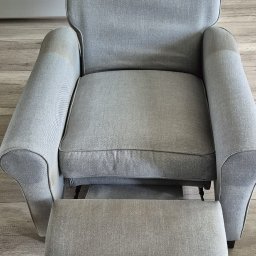 ABSmartClean - Szary fotel z wysuwanym podnóżkiem, widoczne plamy na podłokietnikach, sugerujące świeżo wykonane czyszczenie tapicerki. W tle odkurzacz piorący.