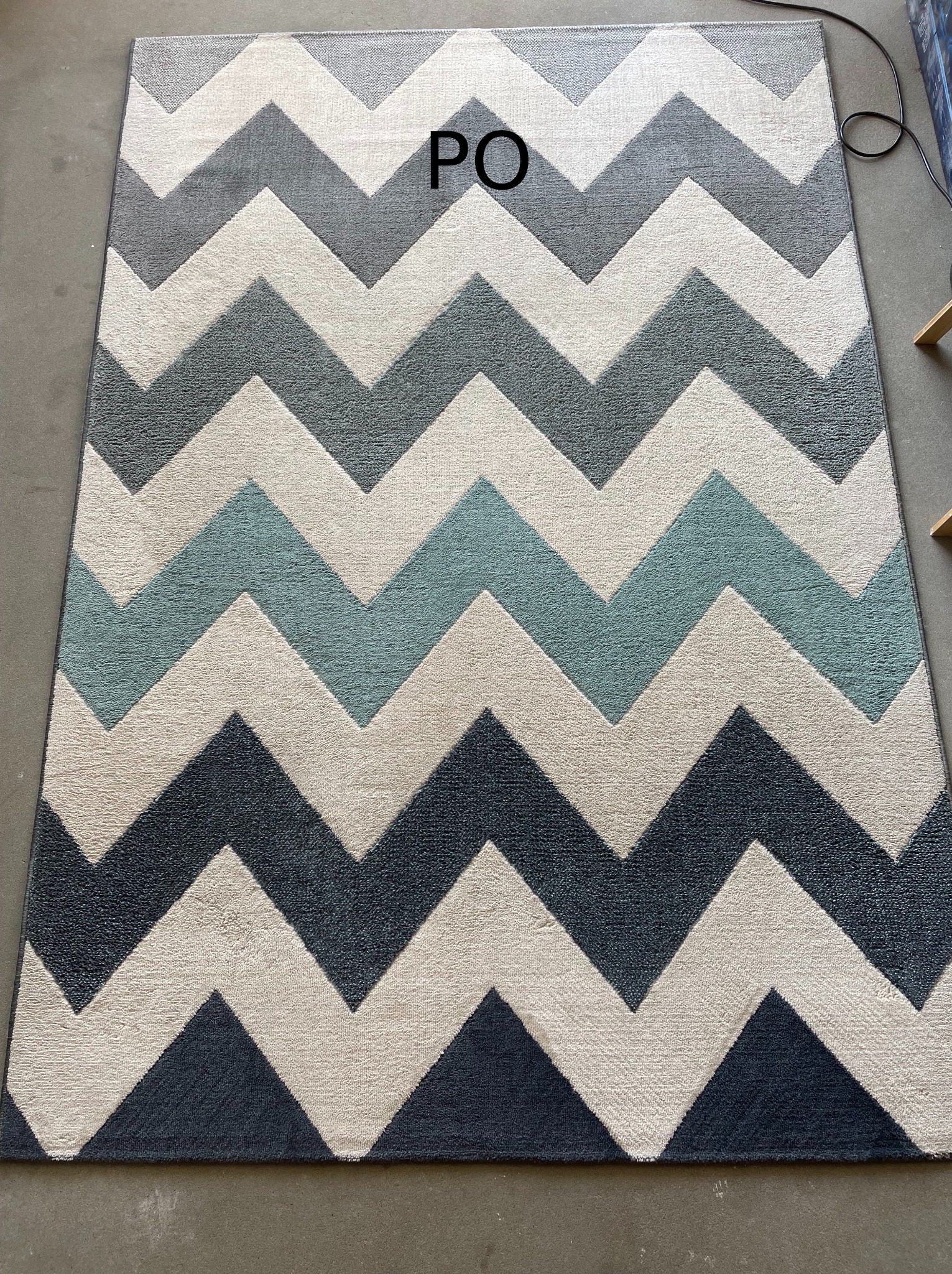 Wyczyszczony dywan w zygzaki, odświeżony po praniu, z widocznym napisem 'PO' sugerującym efekt końcowy usługi czyszczenia.