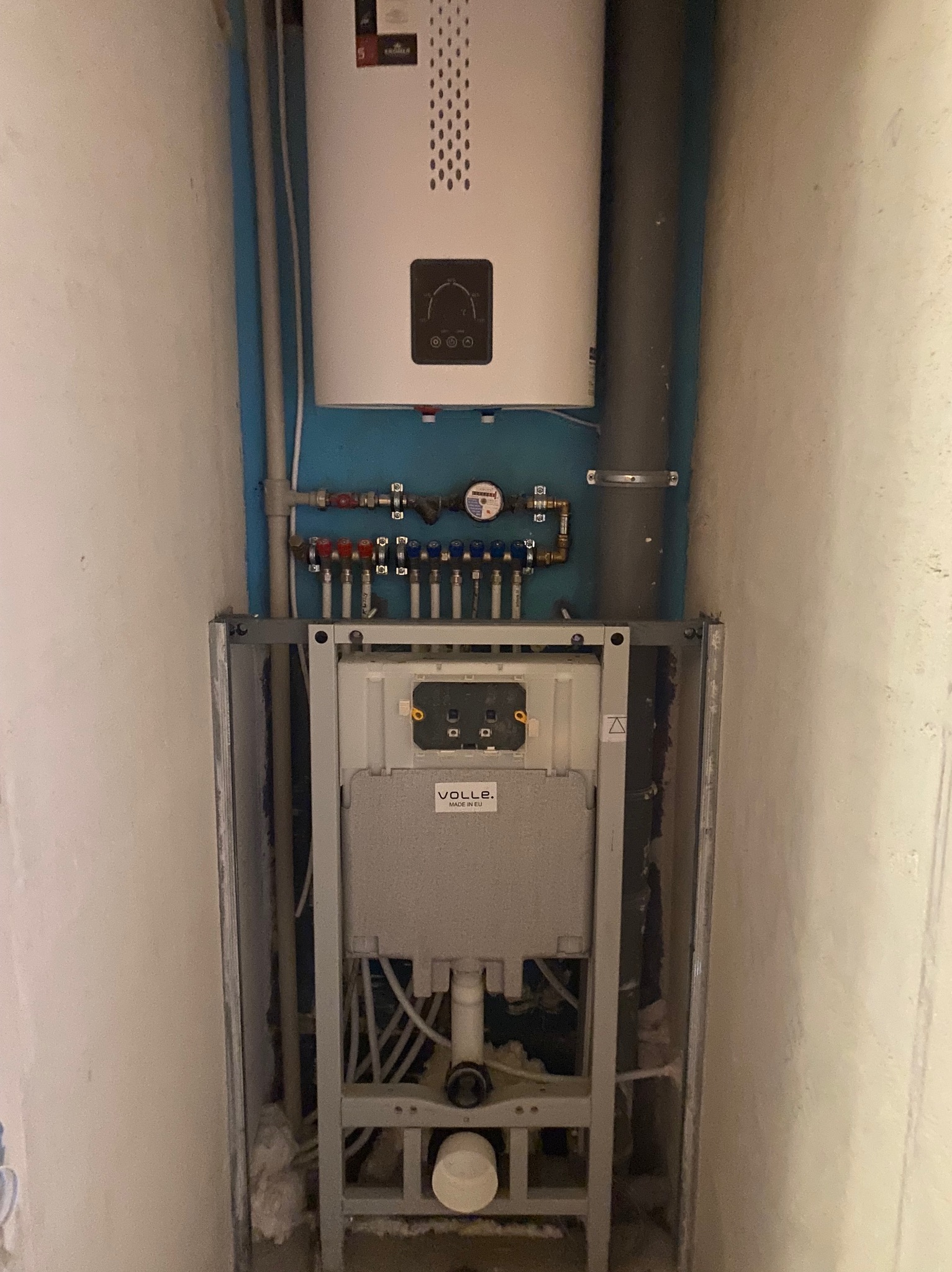 Instalacja wodno-kanalizacyjna w zabudowie stelażowej z widocznym bojlerem i rozdzielaczem, umieszczona w wąskiej wnęce w trakcie prac wykończeniowych.