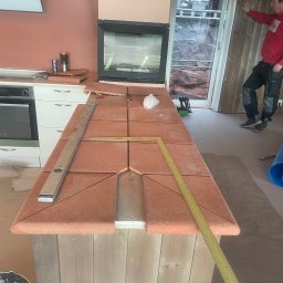 Angel-bud - Blat kuchenny z terakoty w trakcie montażu, widoczne narzędzia: poziomica i miarka. W tle okno i osoba w czerwonej bluzie. Nietypowe wykończenie.