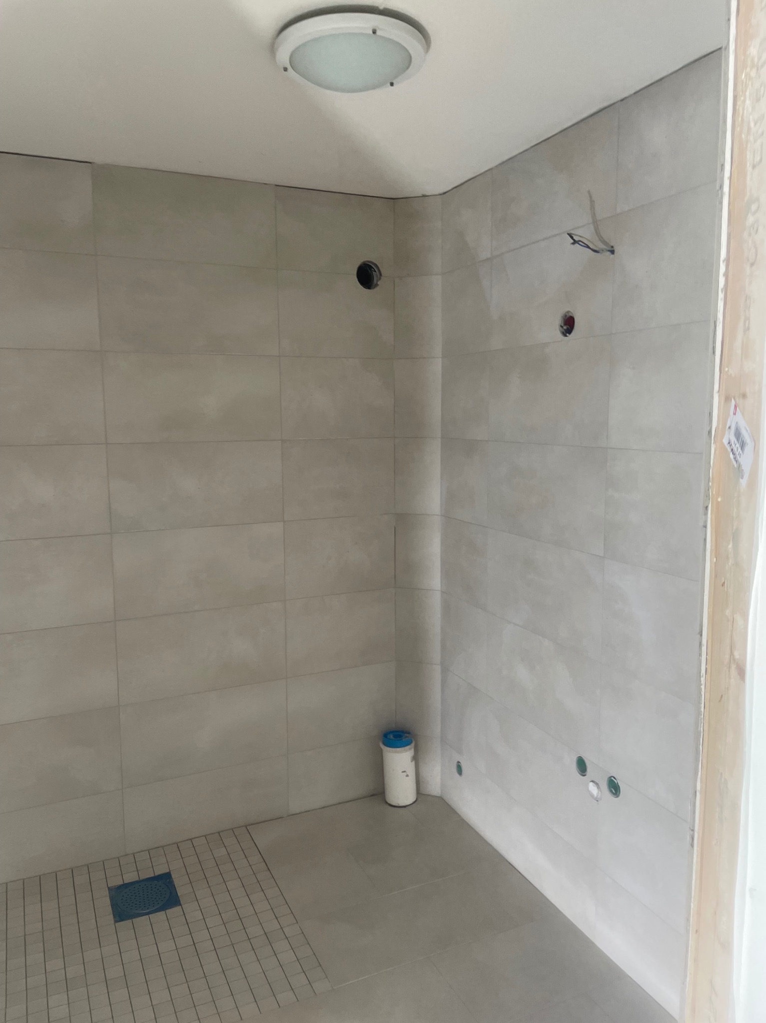 Wykończona łazienka z jasnymi płytkami, widoczne otwory na armaturę i odpływ liniowy. Minimalistyczny design, surowy stan przed montażem wyposażenia.