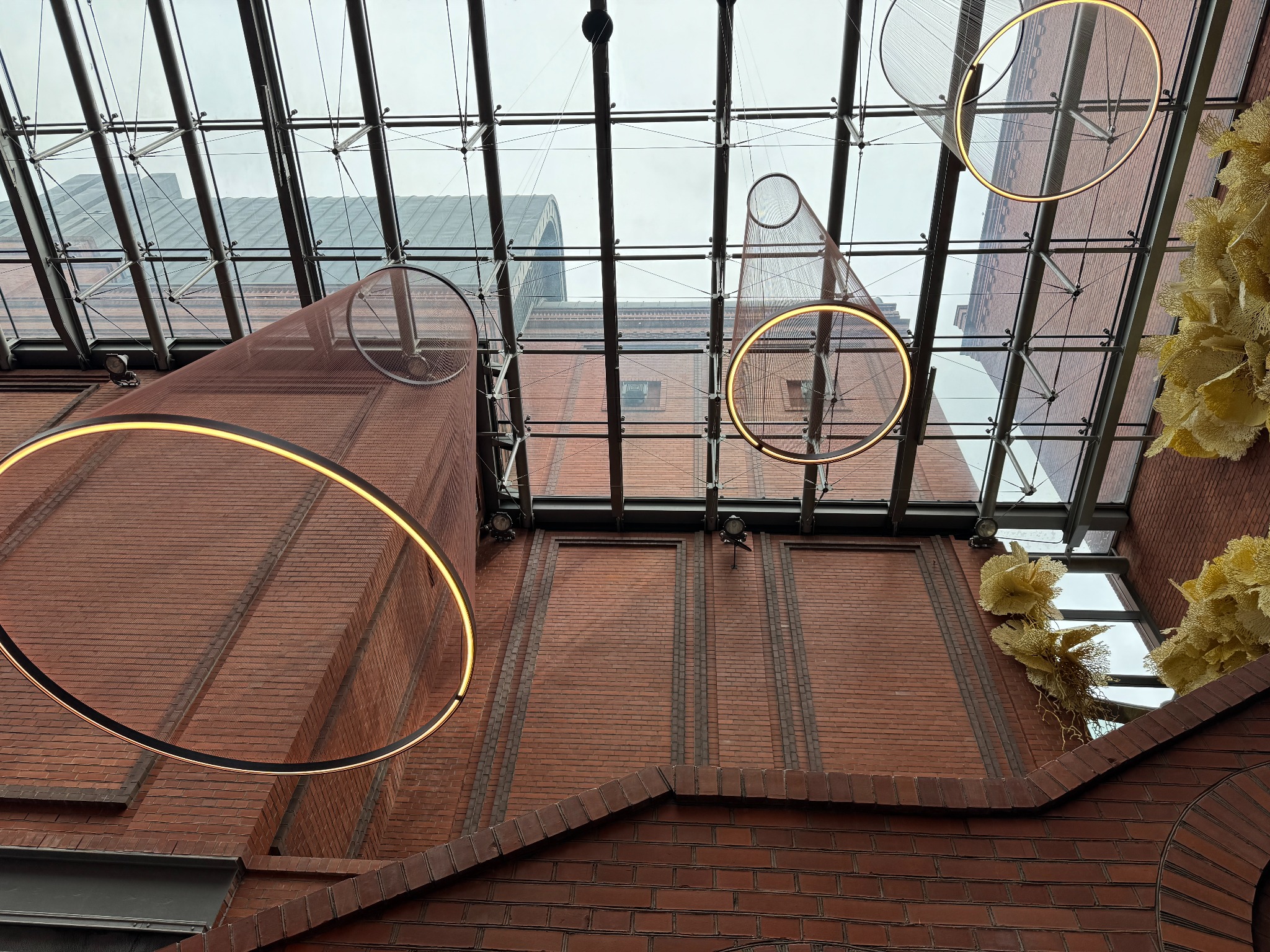 Nowoczesne, okrągłe lampy wiszące z LED na tle ceglanej ściany i szklanego dachu. Nietypowe oświetlenie wnętrza z dekoracjami.