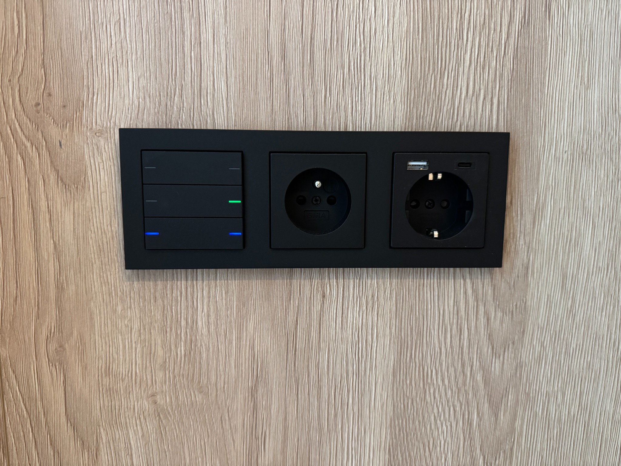 Czarny panel z włącznikami światła, gniazdkiem elektrycznym i USB-C na drewnopodobnej ścianie. Nowoczesny design, minimalistyczny styl, oświetlenie LED.