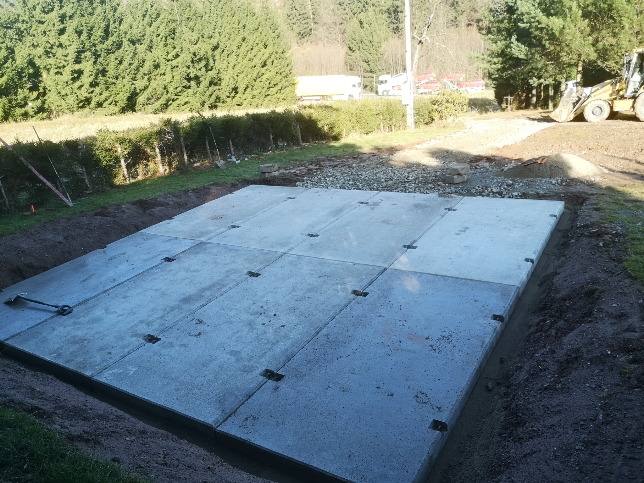 Gotowa płyta fundamentowa z prefabrykatów betonowych na działce, widoczny wykop i maszyna budowlana w tle. Realizacja z użyciem gotowych elementów.