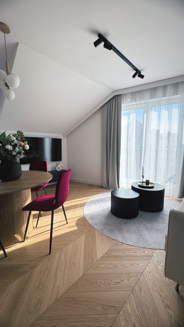 Jasna jodełka na podłodze w salonie z fioletowymi krzesłami i okrągłym dywanem. Ukośny sufit z oknem i światłem dziennym. Nowoczesne oświetlenie sufitowe.