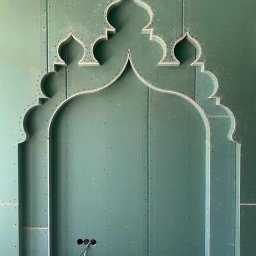 Maksibud - Nietypowa konstrukcja z płyty karton-gips w kolorze zielonym, tworząca dekoracyjny łuk z orientalnymi motywami. Widoczne otwory na gniazdka elektryczne i przewody.