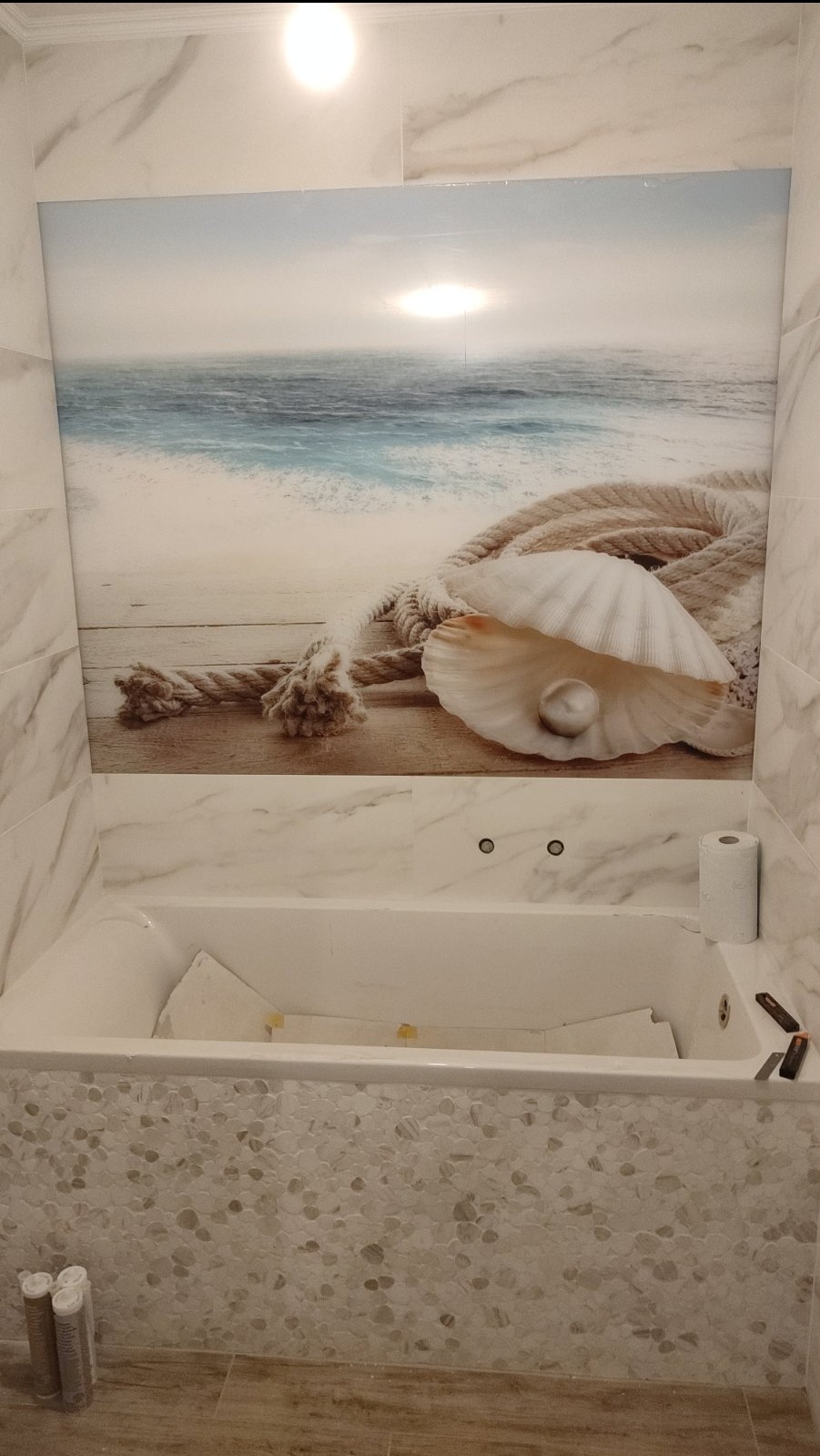 Wykończona łazienka z wanną obłożoną mozaiką i panelem ściennym z motywem morskim. Widoczne narzędzia glazurnicze.