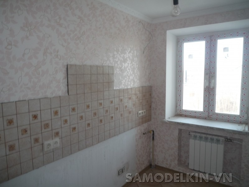 Fragment kuchni w trakcie układania płytek ściennych w beżowym odcieniu, widoczne gniazdka elektryczne i fragment okna z grzejnikiem.