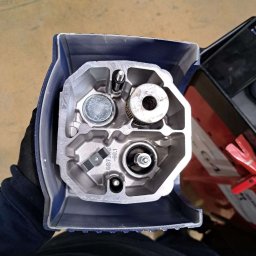 95 Garage - Wnętrze głowicy silnika spalinowego w niebieskiej obudowie, widok z góry. Widoczne elementy mechaniczne i oznaczenia GBT3.0 -50.1. Obok narzędzia serwisowe.