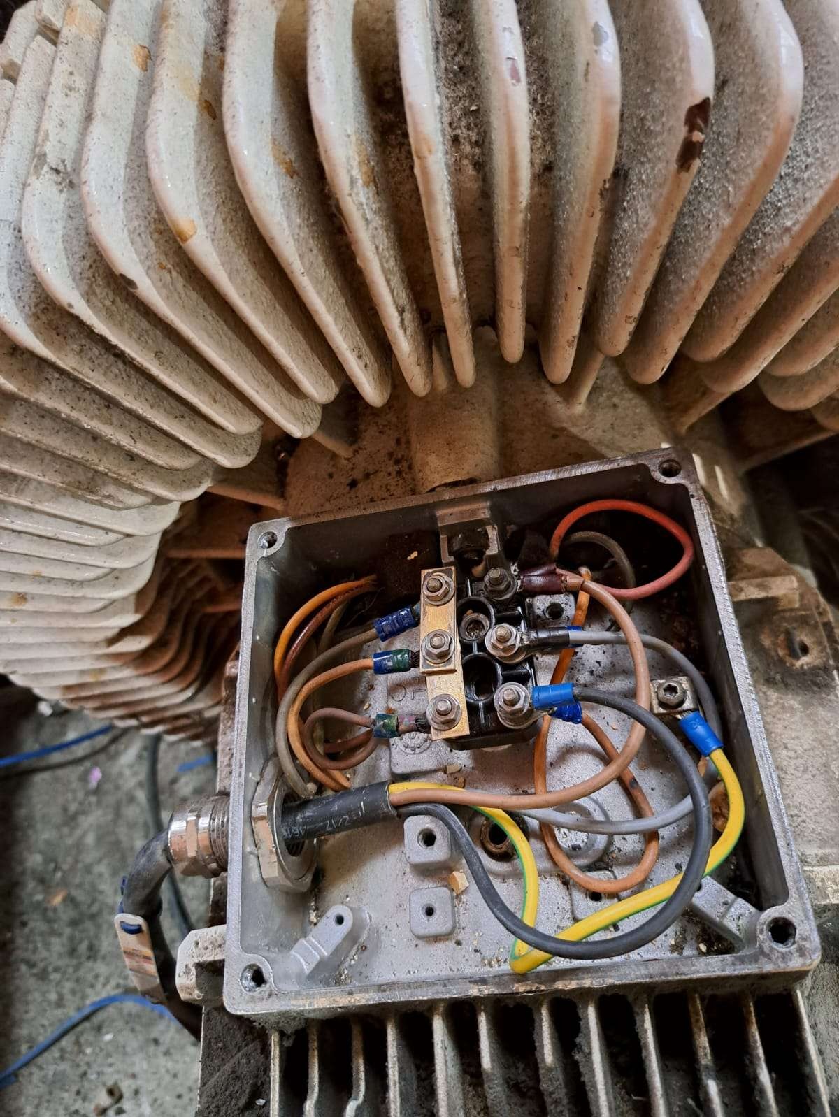 Otwarta puszka elektryczna silnika z widocznymi przewodami i złączkami, ukazująca etap naprawy lub diagnostyki maszyny. Widoczne ślady użytkowania.