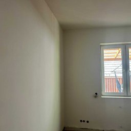 Usługi Remontowo-Wykończeniowe Dawid Wędrzyk - Wnętrze po szpachlowaniu i malowaniu na jasny odcień. Widoczne gładkie ściany, okno z widokiem na zewnątrz i przygotowane punkty elektryczne.