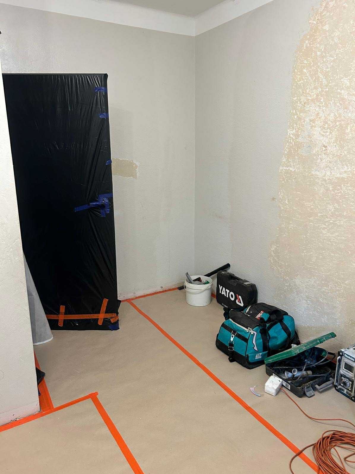 Przygotowanie do prac wykończeniowych: zabezpieczona folią strefa, narzędzia Yato i Makita, wyznaczona taśmą przestrzeń w jasnym pomieszczeniu przed szpachlowaniem.