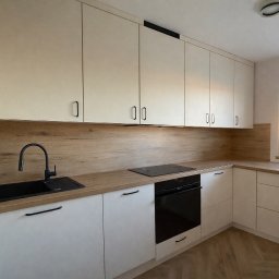 TIMBER CRAFT Krzysztof Windorpski - Jasna zabudowa kuchenna z drewnianym blatem i czarnymi uchwytami, widok z perspektywy. Realizacja w Kołczygłowach.