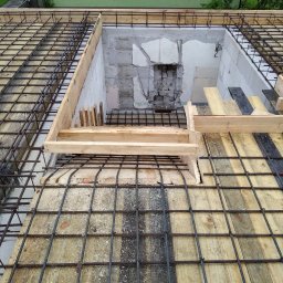 Robert Jórkowski - Zbrojenie stropu z otworem w Łomży, przygotowane do zalania betonem. Widoczne drewniane szalunki i siatka z prętów stalowych. Prace budowlane w toku.