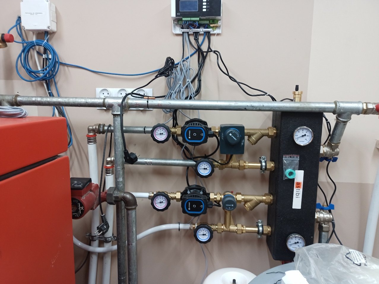 Instalacja centralnego ogrzewania z widocznymi rurami, manometrami i pompami obiegowymi. Elementy połączone, tworzą system grzewczy w pomieszczeniu.