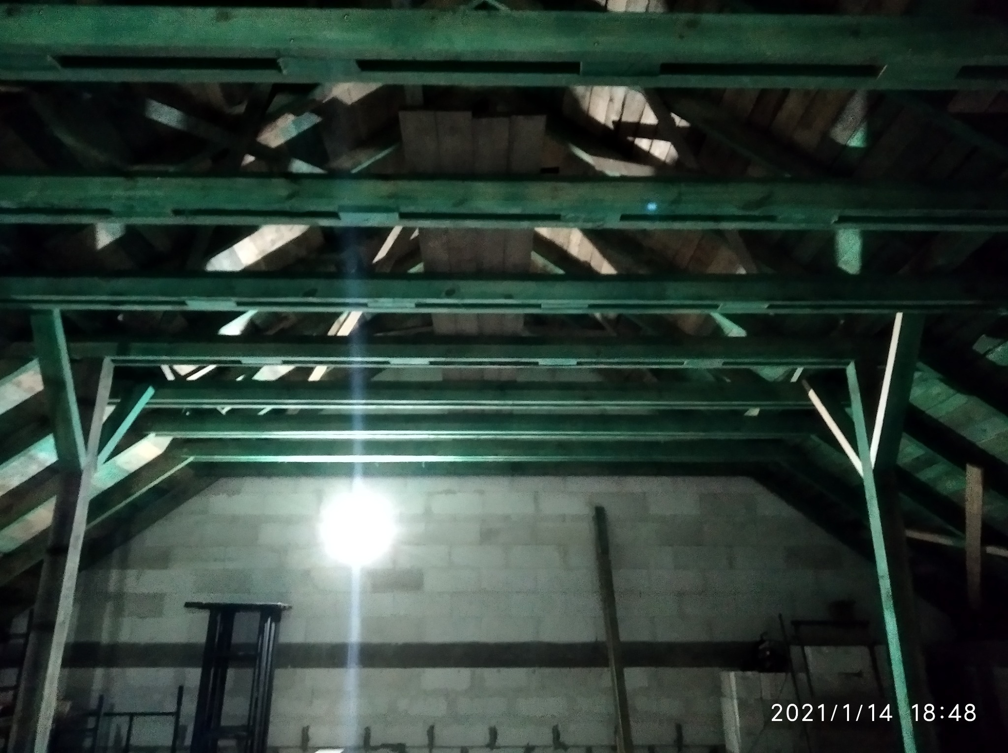 Wnętrze poddasza w trakcie budowy z widoczną konstrukcją drewnianą i ścianami z bloczków. Oświetlenie punktowe. Widoczne elementy rusztowania.