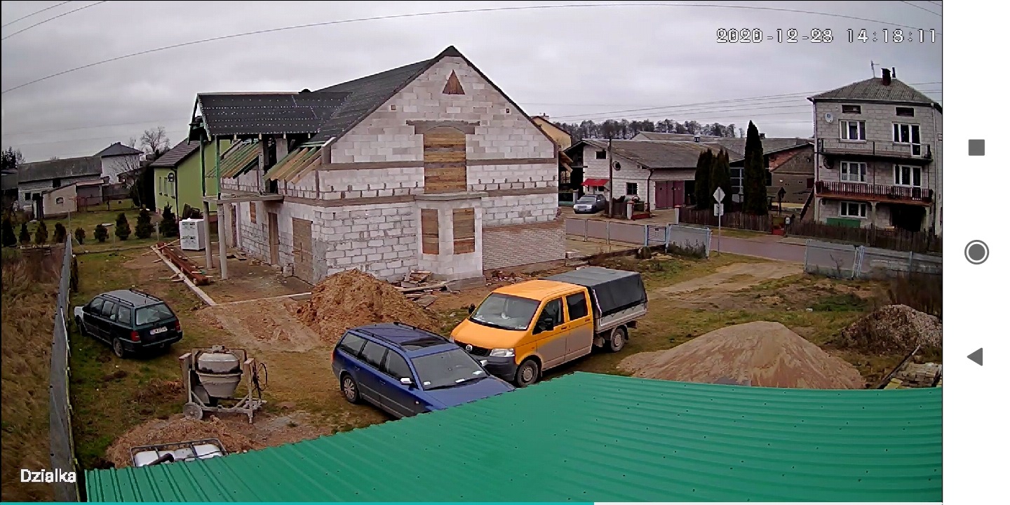 Budowa domu z białego pustaka, częściowo zadaszonego. Na posesji zaparkowane dwa samochody, widoczna betoniarka i hałdy piasku. Ujęcie z góry, z dachu sąsiedniego budynku.