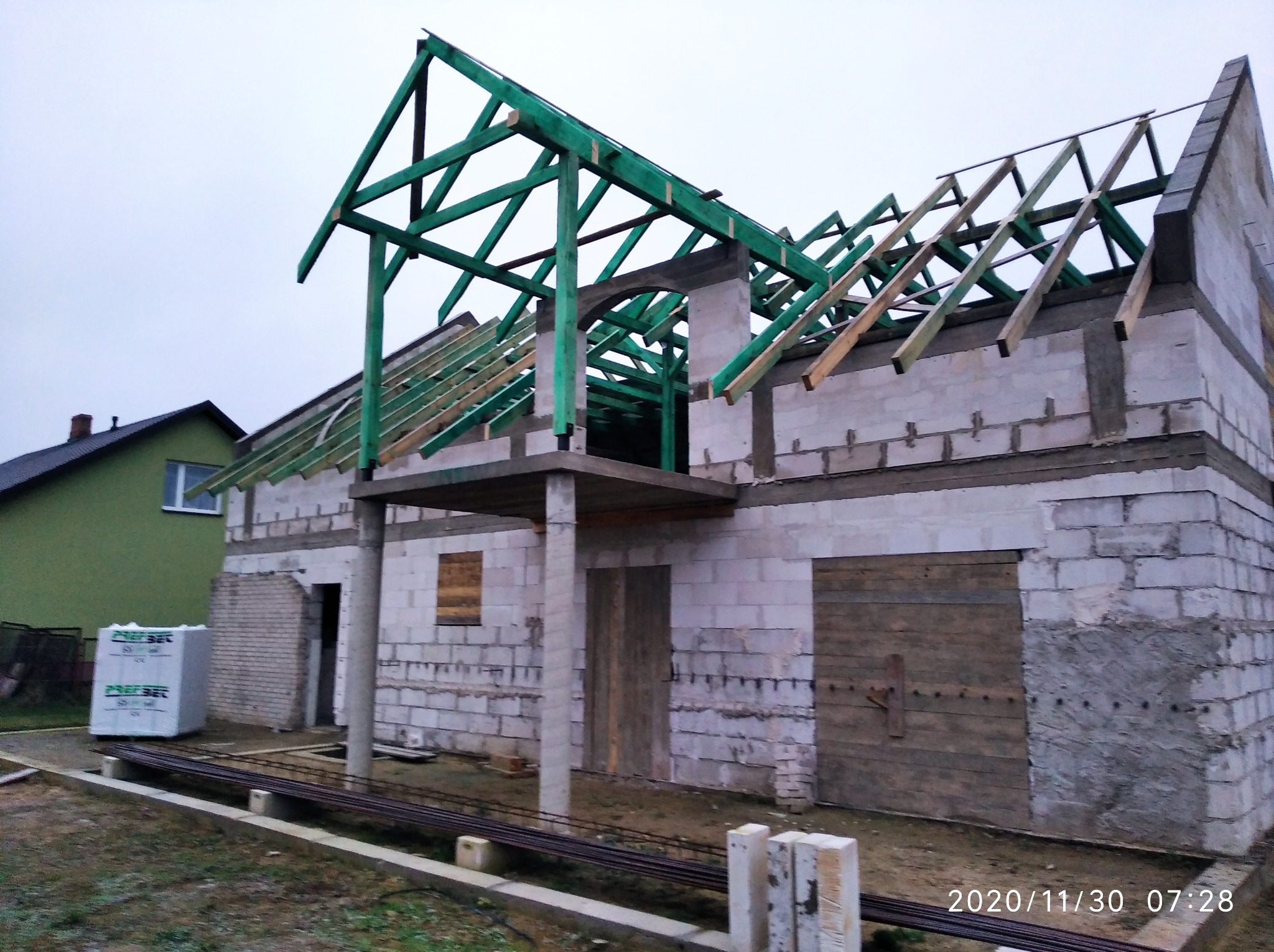 Budowa domu z bloczków: surowy stan z zieloną konstrukcją dachu. Widoczne bloczki, drewniane elementy i przygotowane materiały budowlane. Ujęcie z zewnątrz, w dzień.