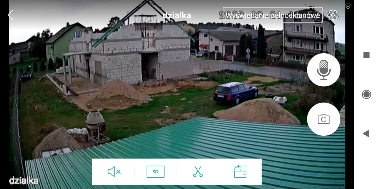 Budowa domu z bloczków, widok z góry na plac budowy z zaparkowanym samochodem. Widoczna betoniarka i hałdy piasku. Ujęcie z kamery monitoringu.