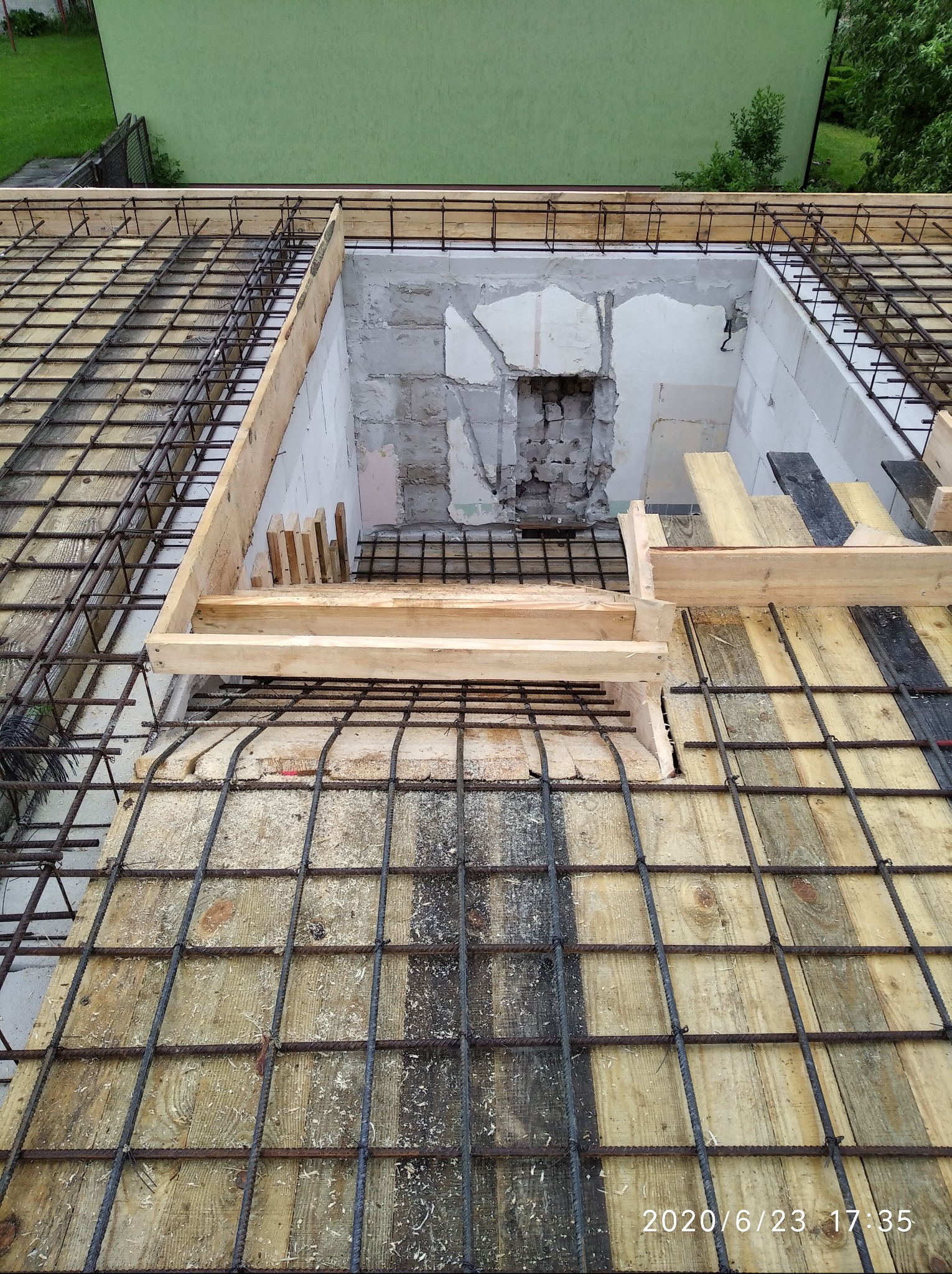 Zbrojenie stropu z otworem w Łomży, przygotowane do zalania betonem. Widoczne drewniane szalunki i siatka z prętów stalowych. Prace budowlane w toku.