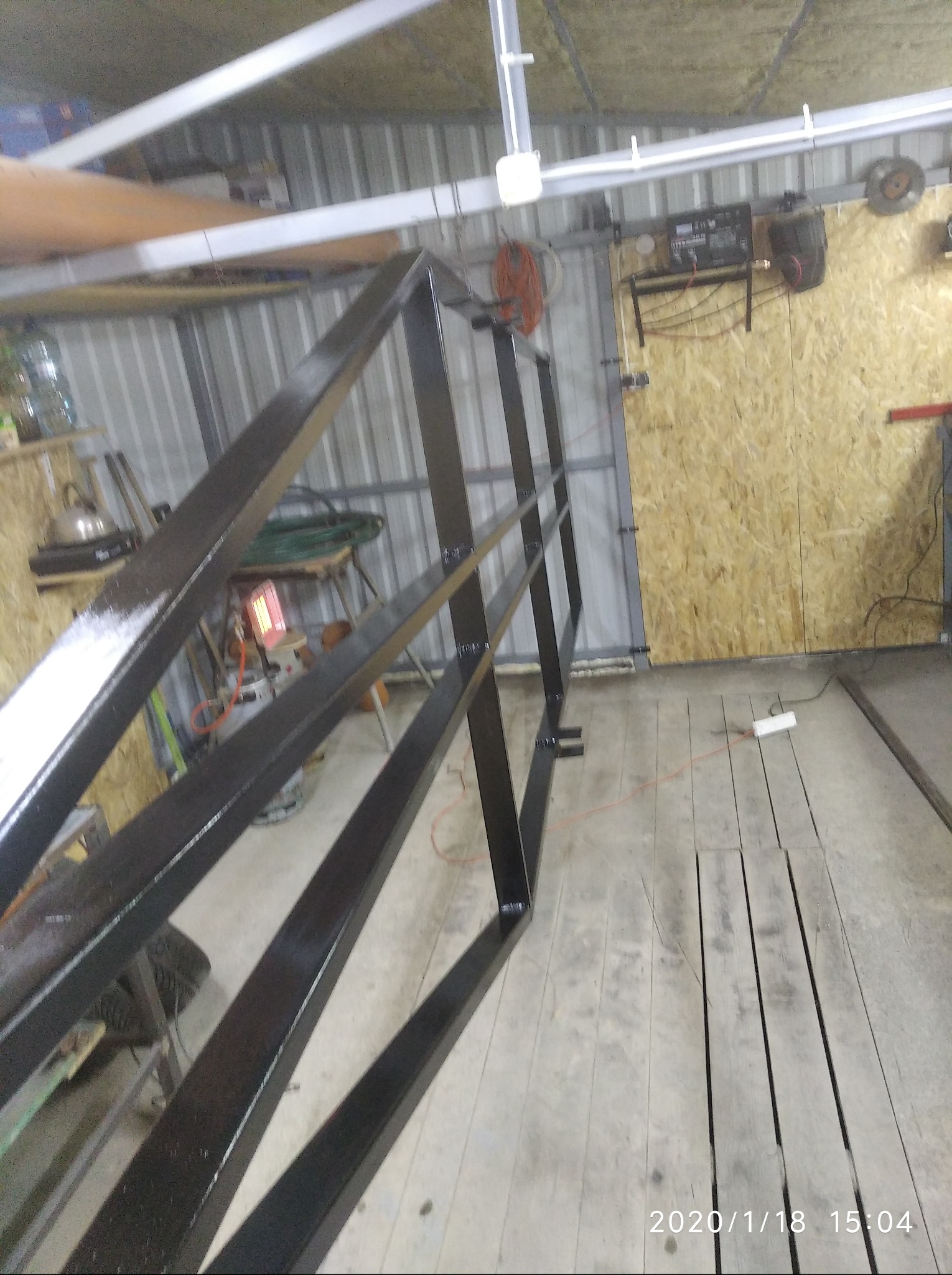 Metalowa konstrukcja pomalowana na czarno, ustawiona w warsztacie. Widoczne narzędzia i elementy wyposażenia warsztatu w tle.