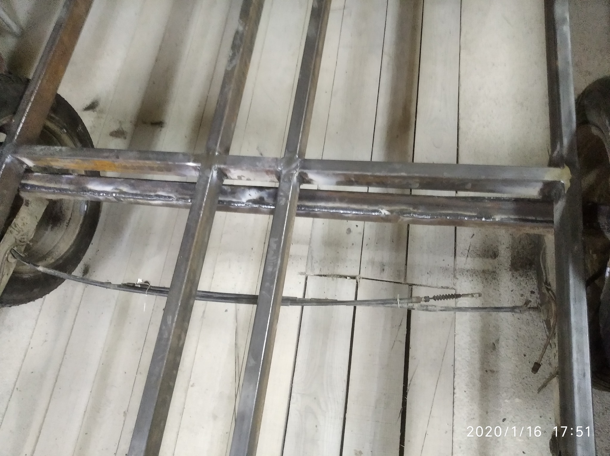 Spawana, metalowa konstrukcja ramy na drewnianej podłodze. Widoczne spawy i elementy zawieszenia. Ujęcie z dołu, podkreślające solidność wykonania.