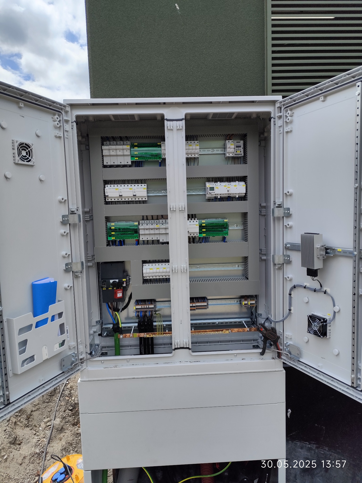 Otwarta szafa sterownicza z widocznymi elementami instalacji elektrycznej, zabezpieczeniami i okablowaniem. Widoczne narzędzia monterskie.